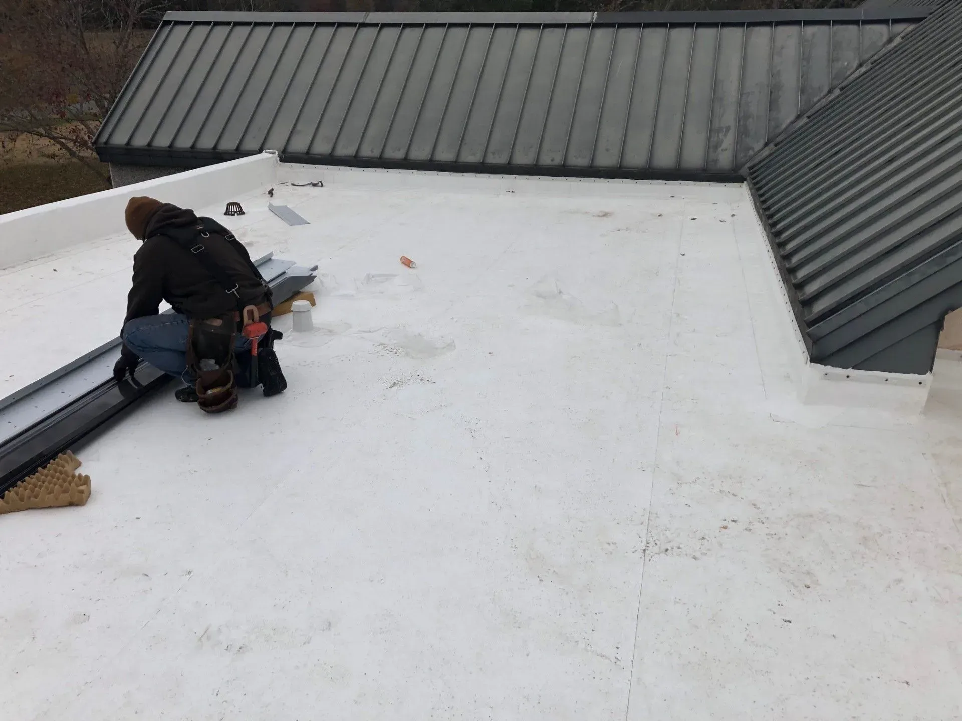 Worker on a flat rooftop applying material near a metal roof edge