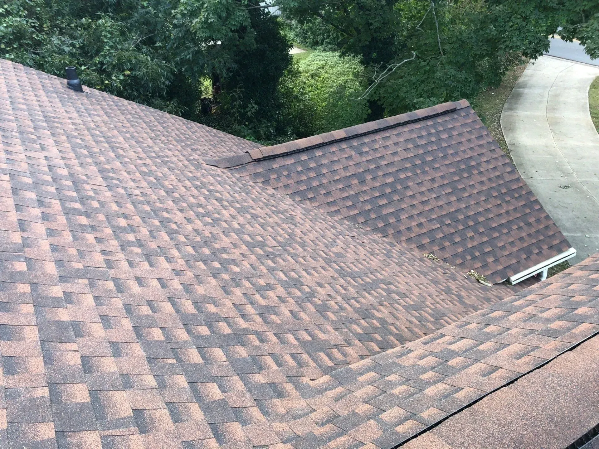 Brown shingle roof with valley and nearby trees beside a curved driveway
