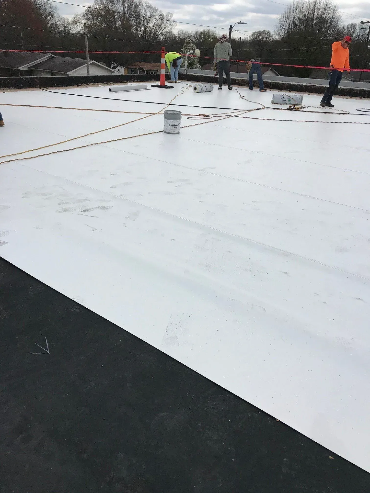 Workers in orange vests on a white rooftop, inspecting a flat roof under cloudy skies.