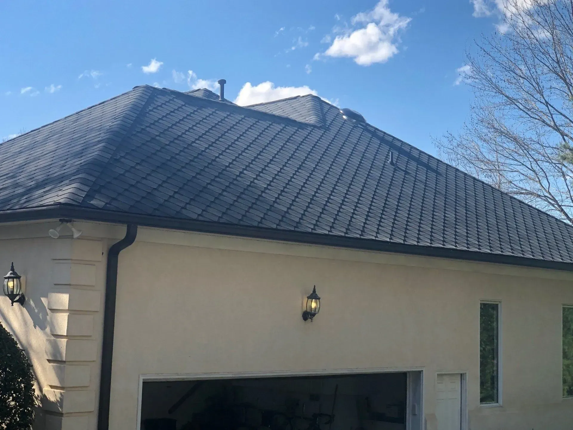 Beige house with dark tiled roof and garage under a blue sky with clouds