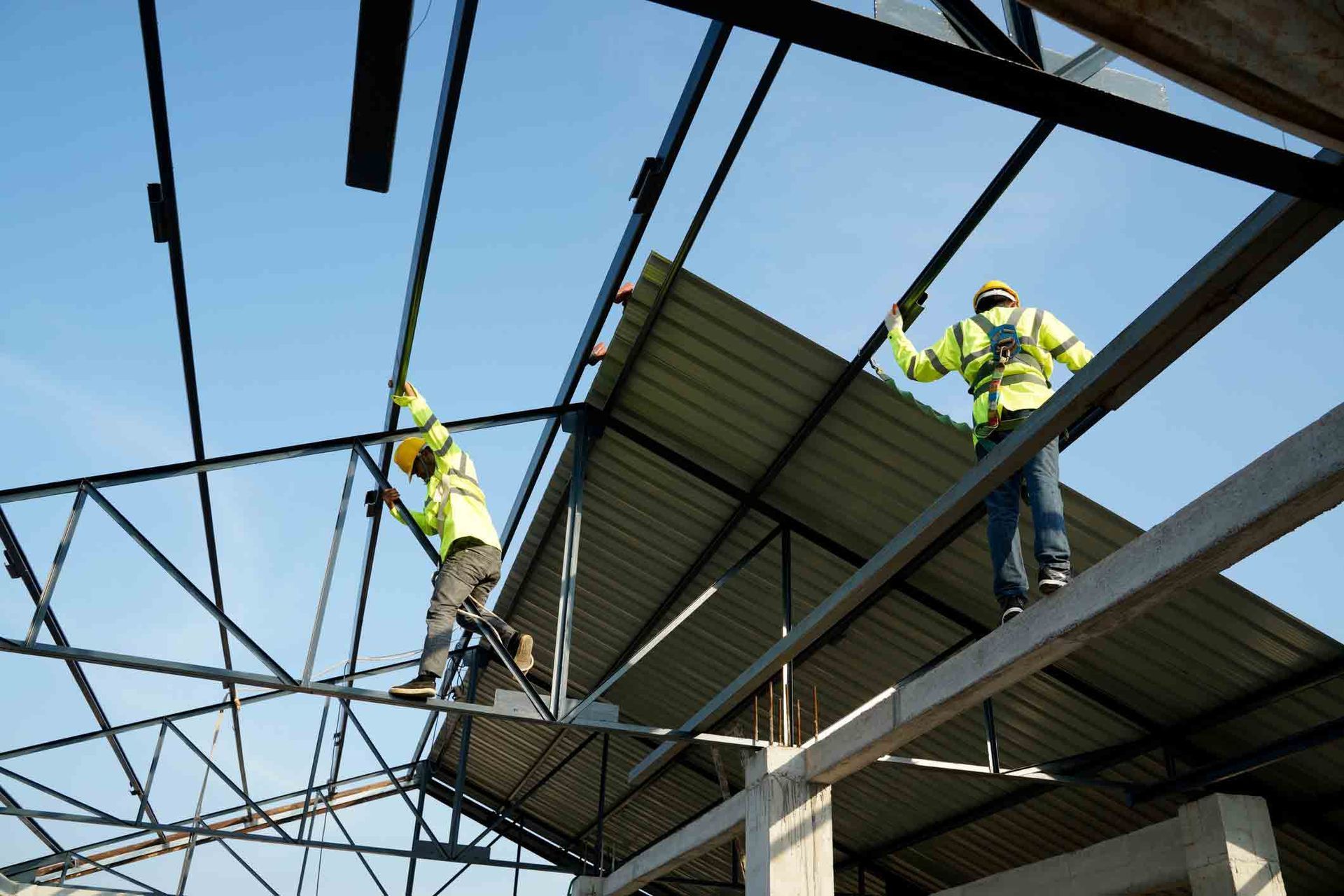 Workers in neon safety vests installing a steel roof frame above a building site