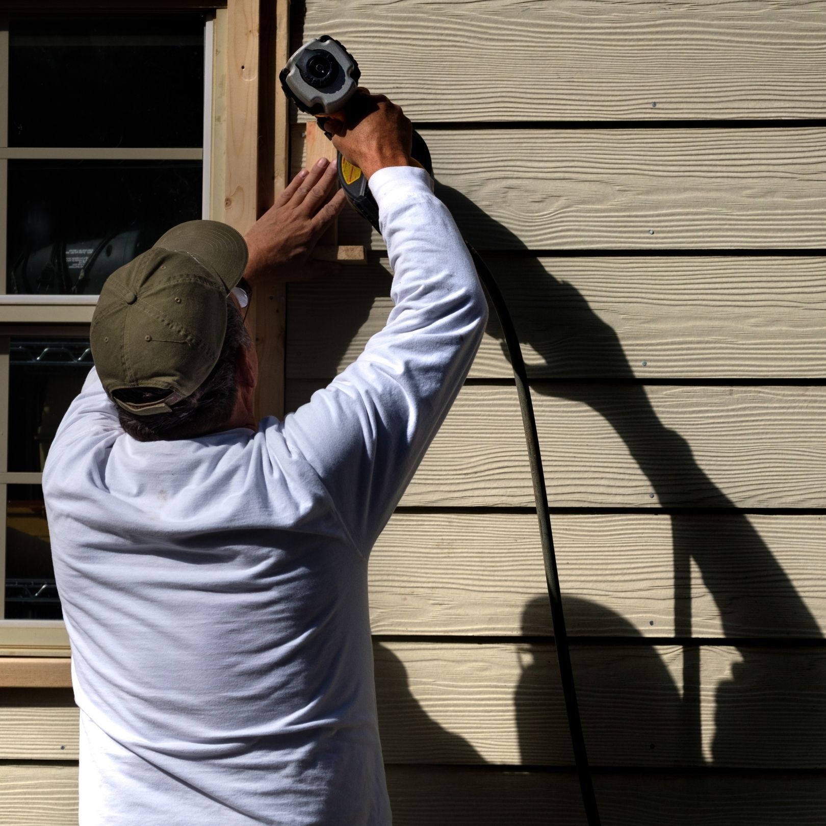 Person using a drill to install trim on tan house siding next to a window