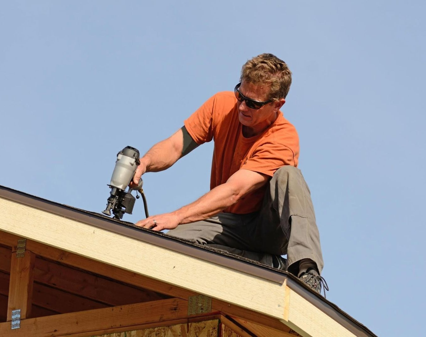 Worker in yellow hard hat repairing a roof with a power tool under a blue sky