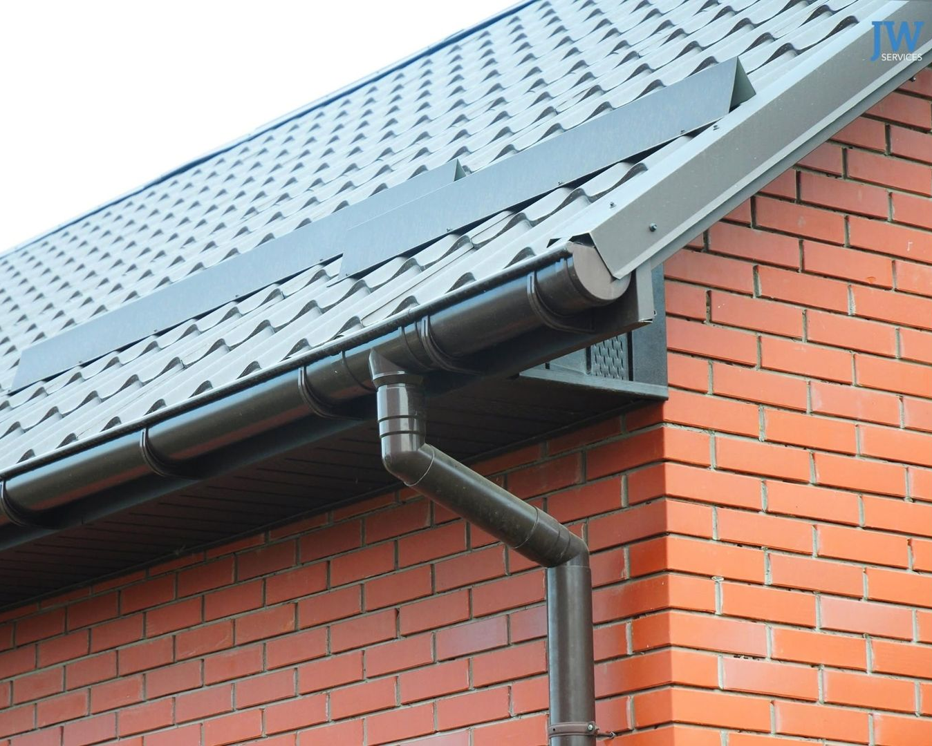 Brown rain gutter and downspout on a corrugated metal roof and wall of a building