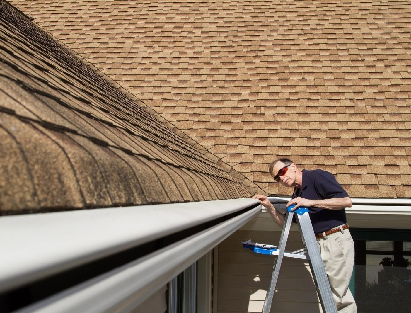 Close-up of a gray asphalt shingle roof ridge beside a house gutter and white trim