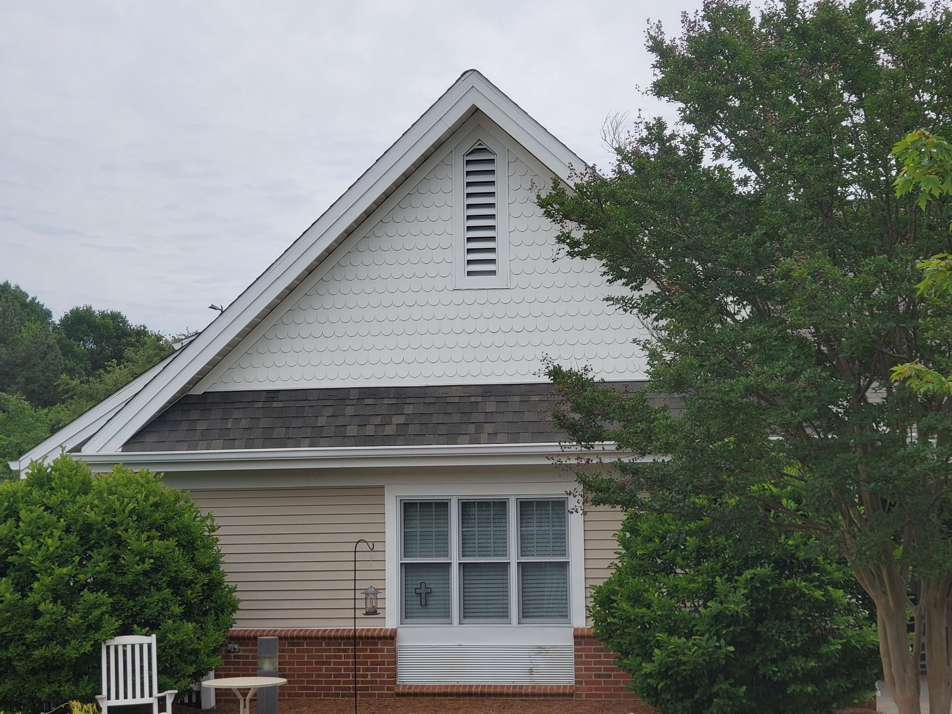 House exterior with white gable, beige siding, and a tree in front under cloudy sky