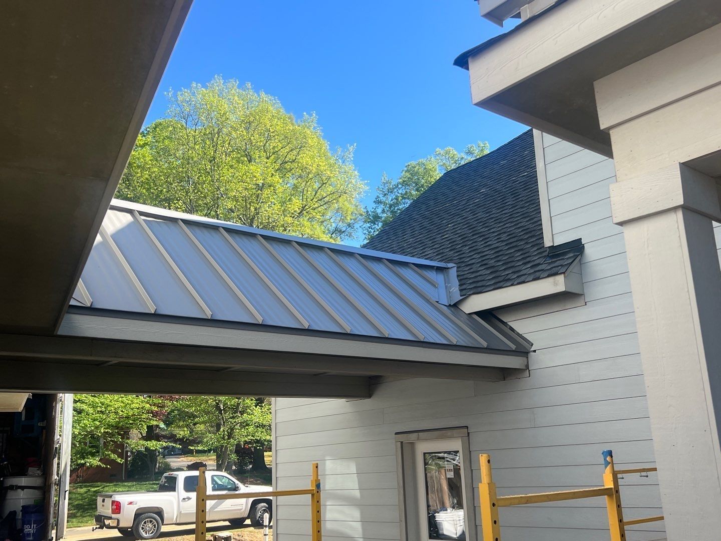 Covered walkway between buildings with a metal roof, white siding, and a truck in the background.