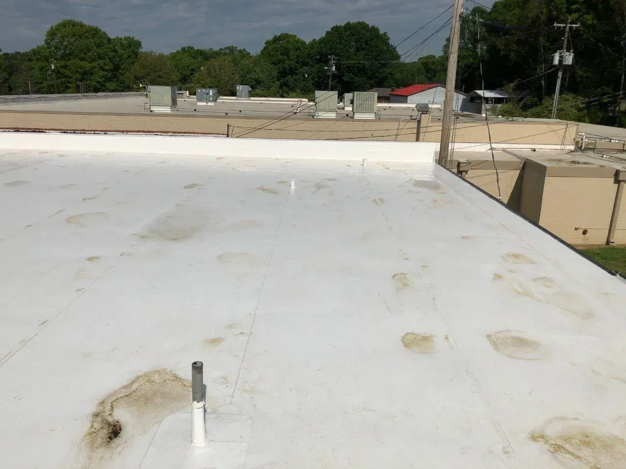 White flat rooftop with vents, overlooking nearby buildings and trees under a clear sky