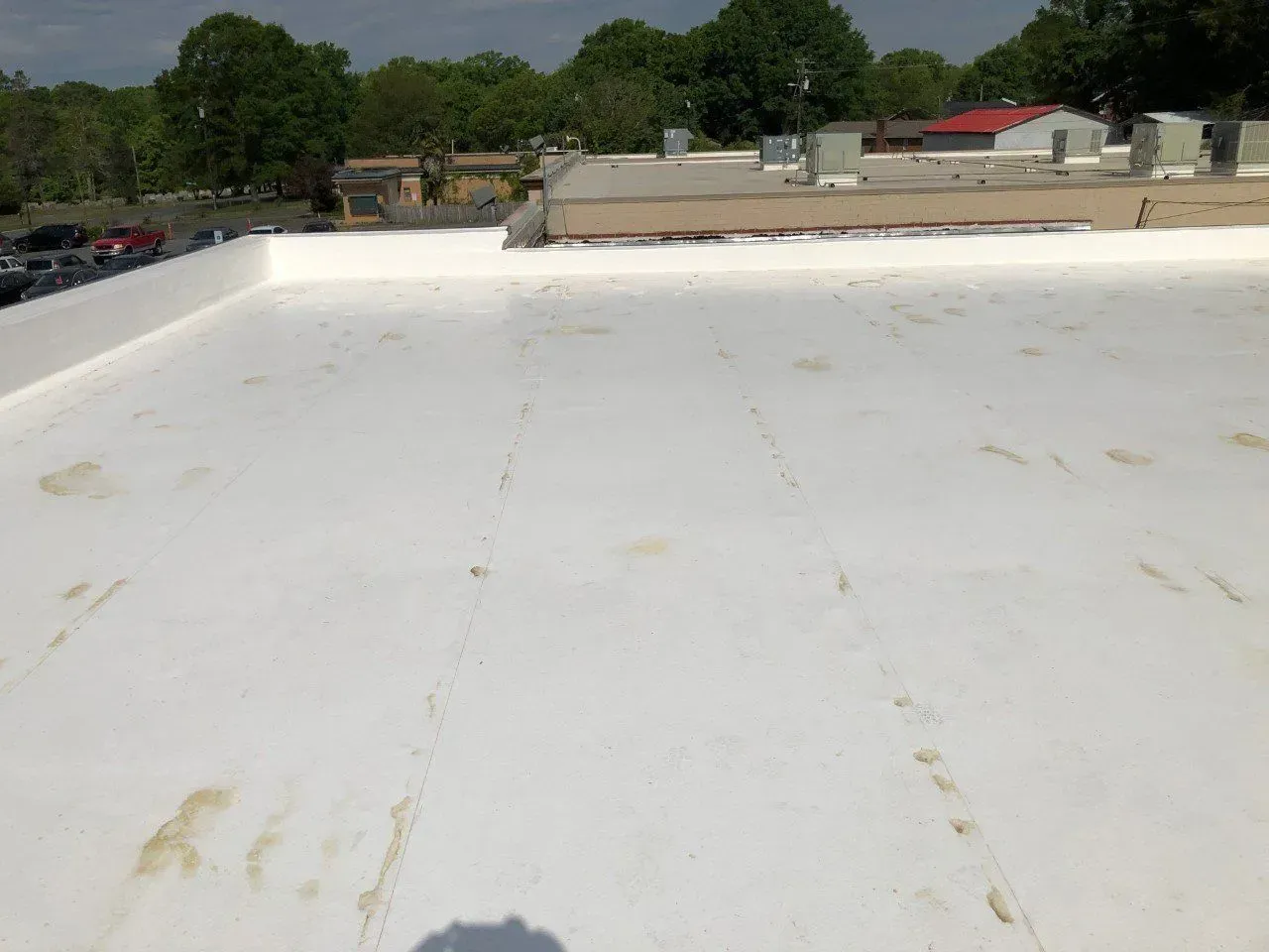 White flat rooftop with faint stains, overlooking trees and low buildings under a clear sky.
