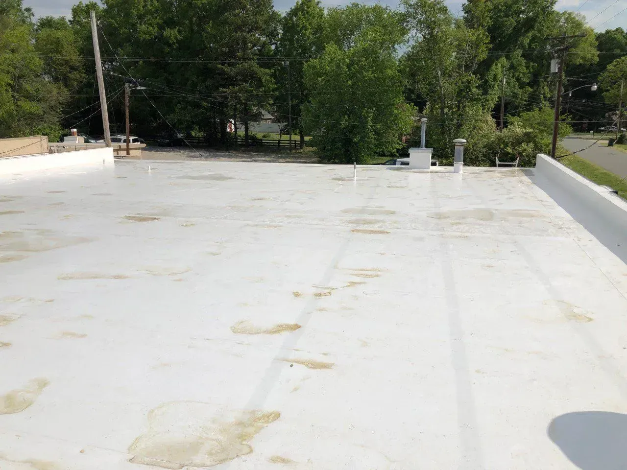 White rooftop with vents and trees in the background on a sunny day
