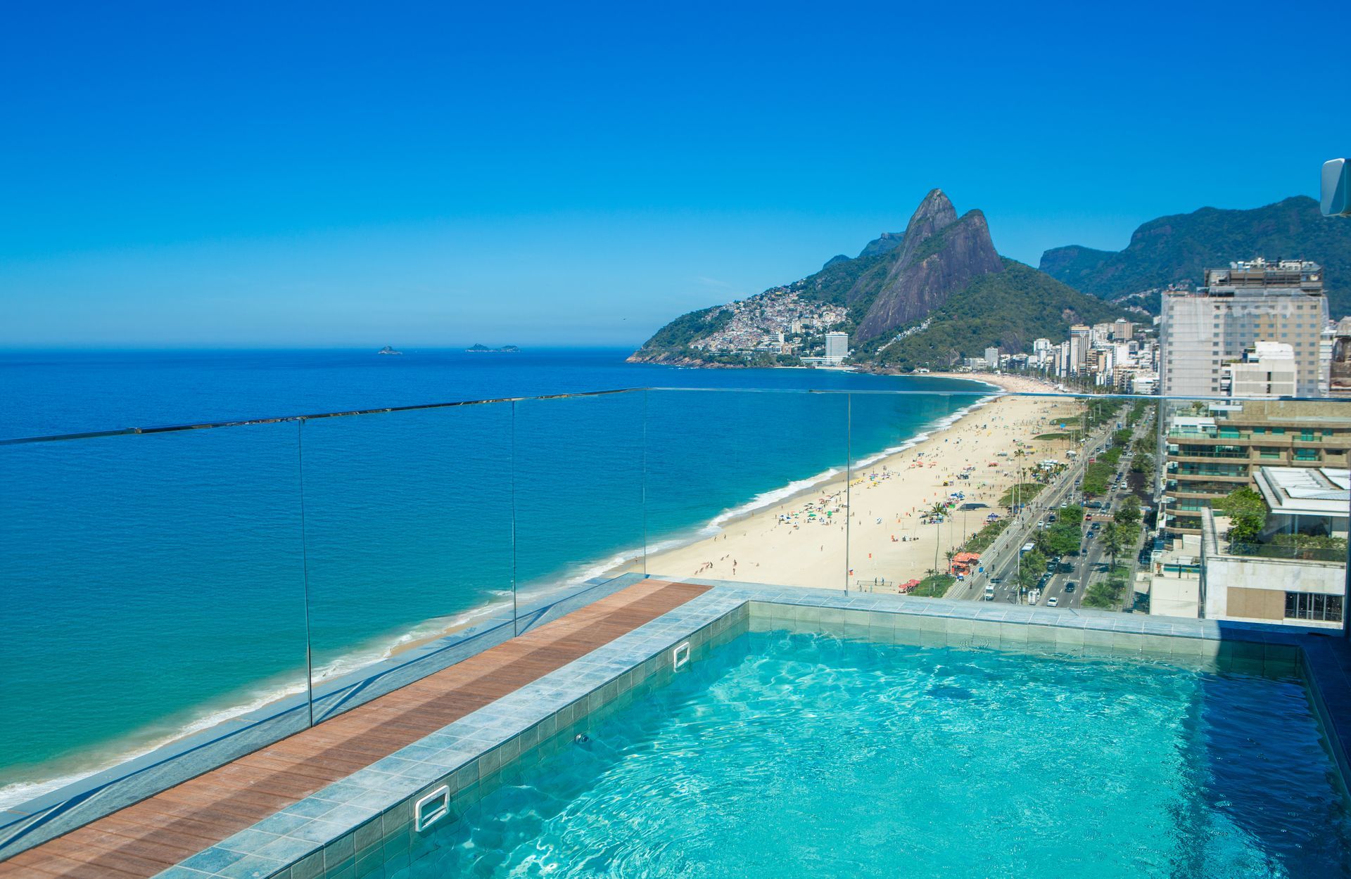 Piscina na cobertura com vista para a praia de Ipanema, no Rio de Janeiro; água azul, dia ensolarado, montanha ao fundo.