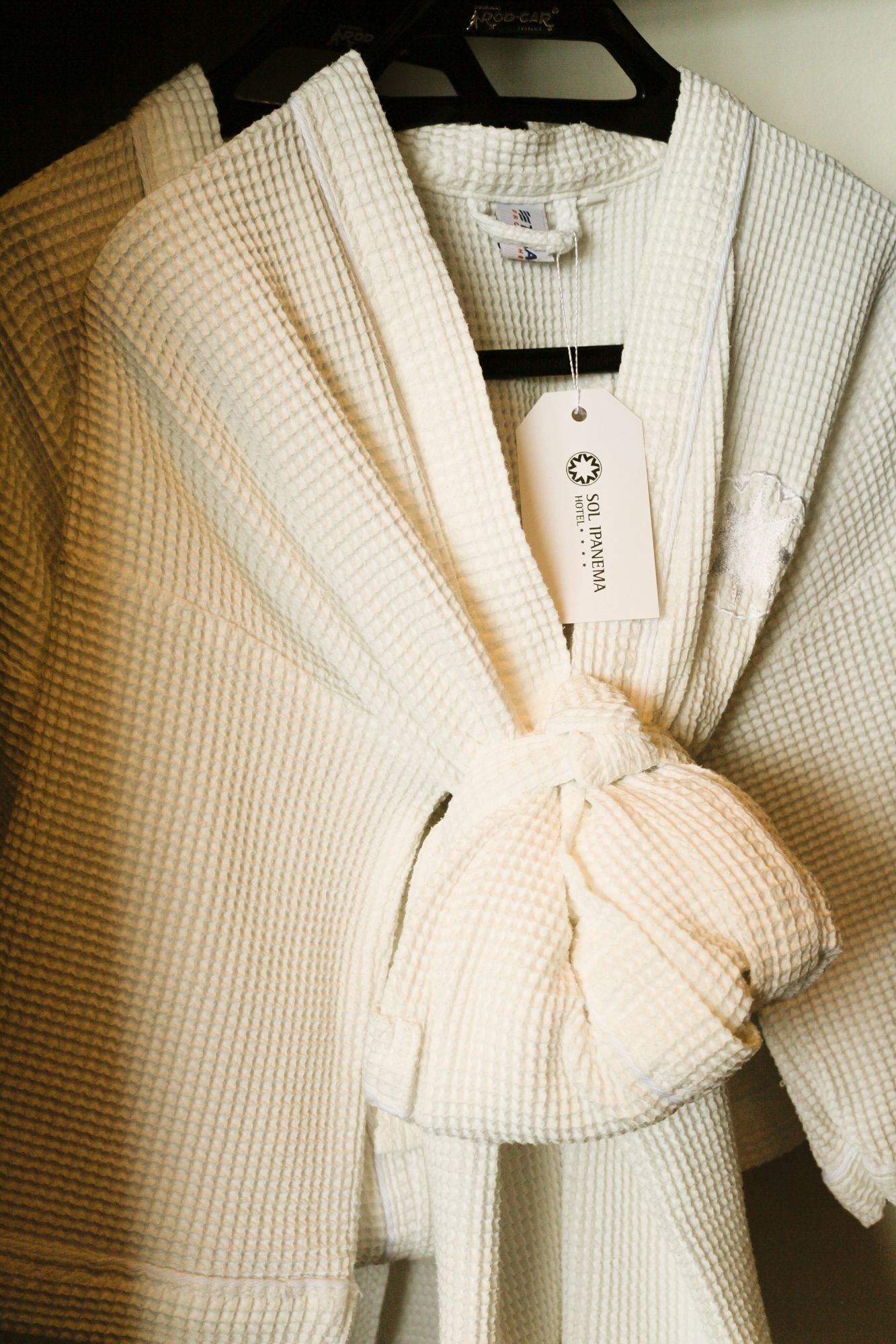 Robe branco de trama waffle pendurado em um cabide preto, amarrado na cintura.