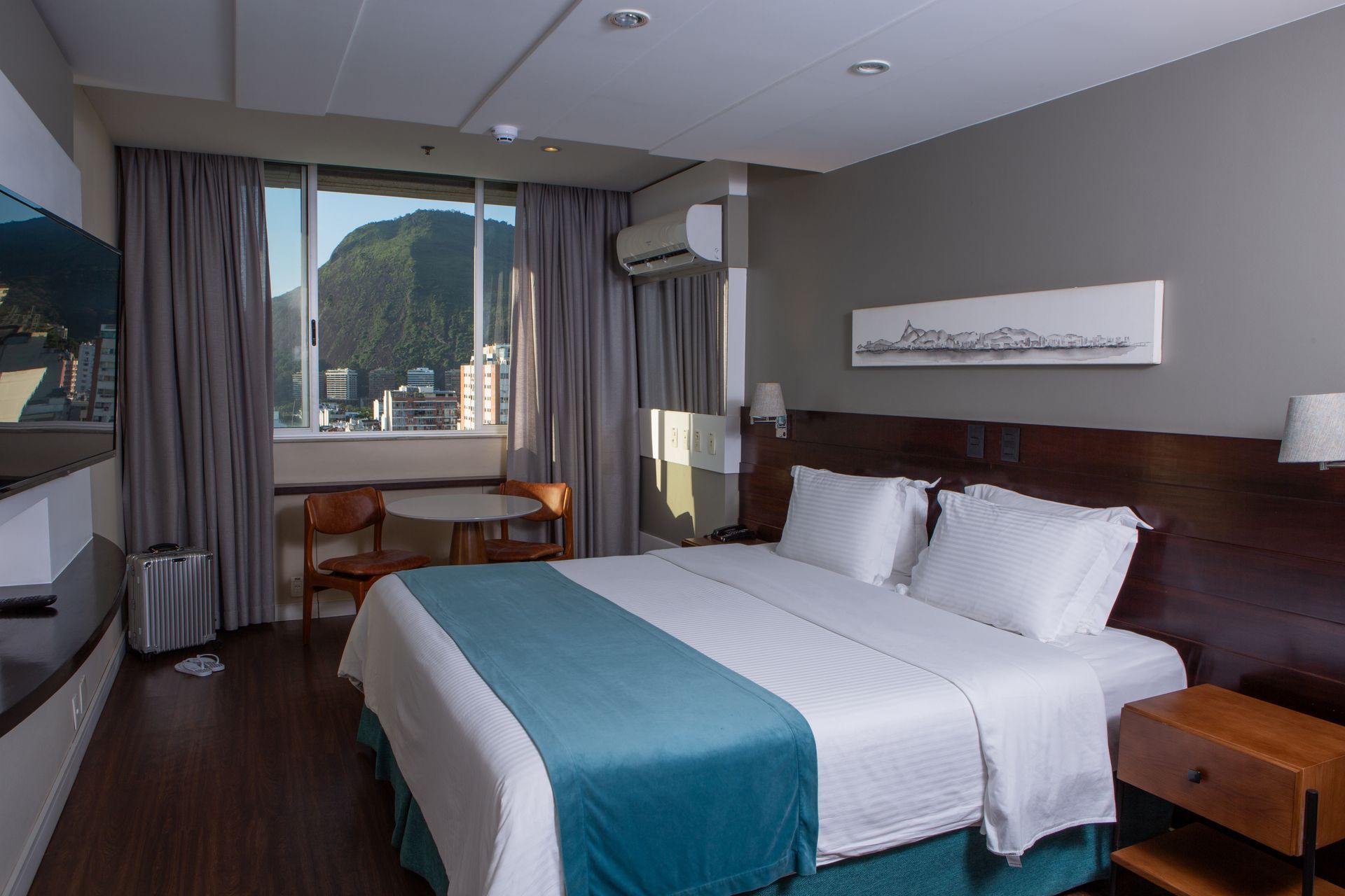 Quarto de hotel com cama, janela com vista para as montanhas e uma pequena área de estar.