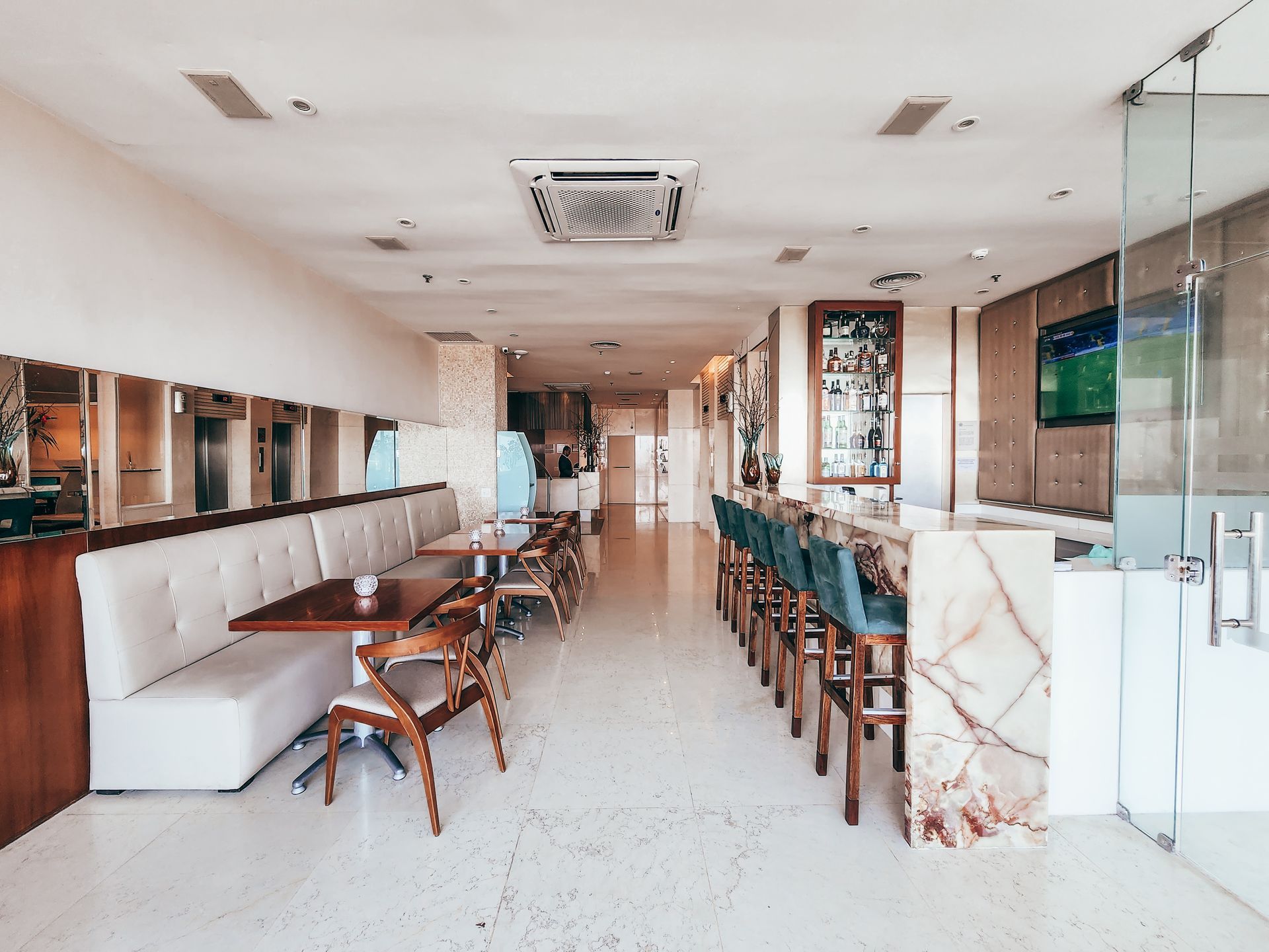Interior de um restaurante moderno com mesas, cabines, bar e uma tela de TV exibindo um jogo esportivo.