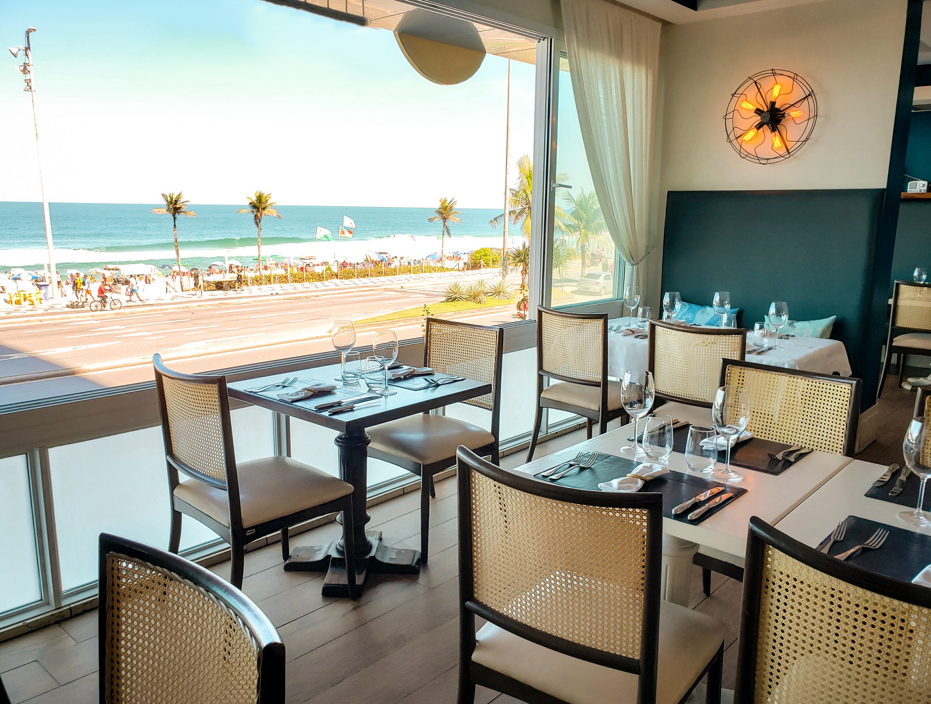 Interior do restaurante com mesas dispostas para jantar, com vista para a praia e o oceano.