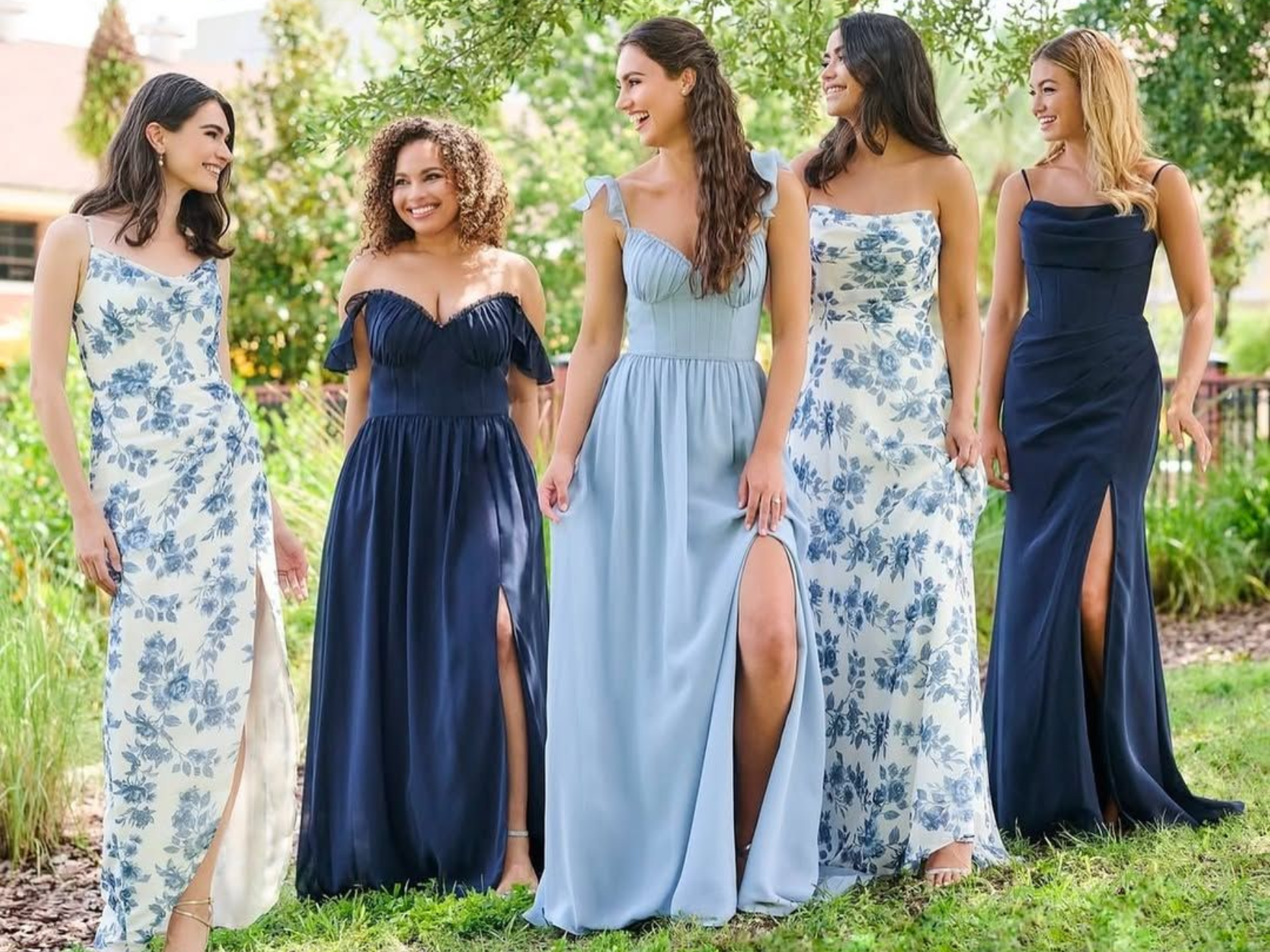 Five women in flowing gowns of blue shades standing outdoors.
