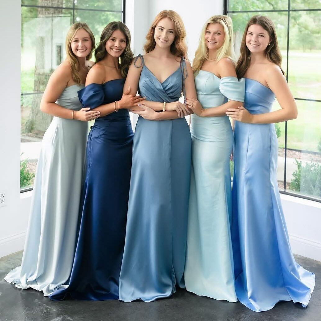 Five women in blue satin gowns, posing in front of a window.