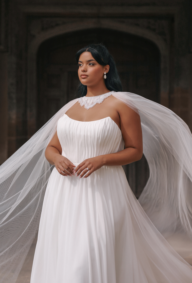Woman in a white off-the-shoulder wedding dress stands outdoors on a brick path.