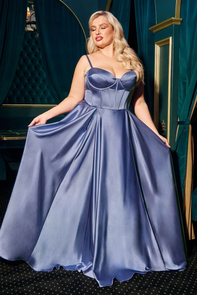 Woman in a long, blue satin gown with a corset bodice, standing in a room with teal curtains.