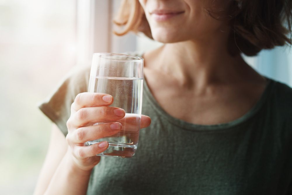 A Woman is Drinking a Glass of Water in Front of a Window — Hinterland Water Cartage in Mooloolah Valley, QLD