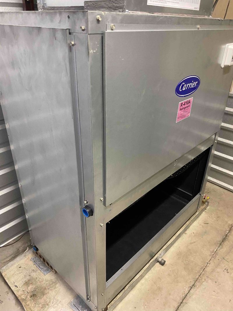 Stainless steel HVAC unit beside a wall, with an open lower access panel.