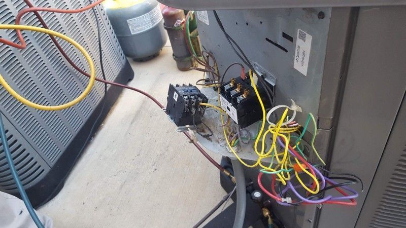 Electrical panel with colorful wires and relays mounted beside HVAC equipment on a concrete floor