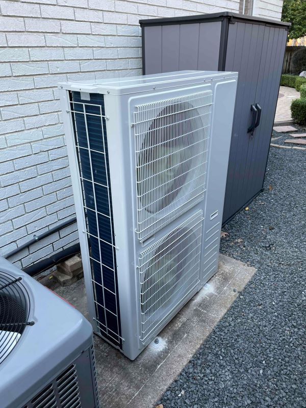 Outdoor air conditioner condenser unit beside a house wall and storage shed on gravel