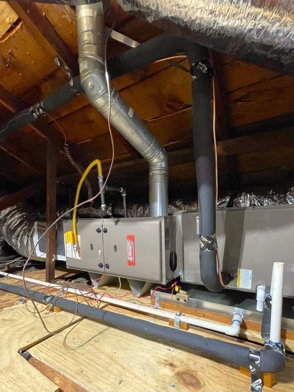 HVAC ductwork and furnace units installed in an attic with exposed insulation and wooden rafters