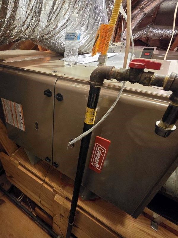 Gray HVAC unit in an attic with insulated ducts, black piping, and a water bottle on top