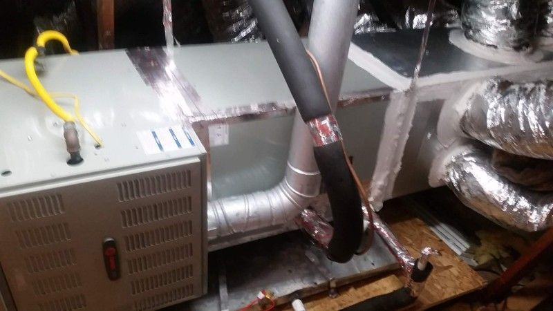 Metal HVAC ducts and insulated pipes in a cramped mechanical space, with a white vented unit and yellow wire.