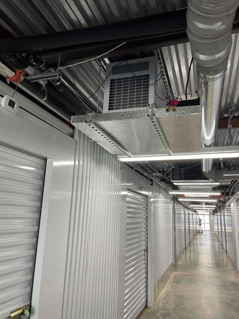 Interior storage hallway with white roll-up doors, exposed ducts, and a long concrete floor corridor