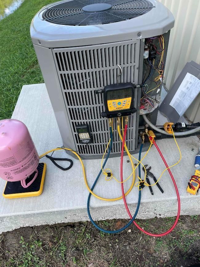 Outdoor air conditioner unit with open service panel and test gauges on a concrete slab