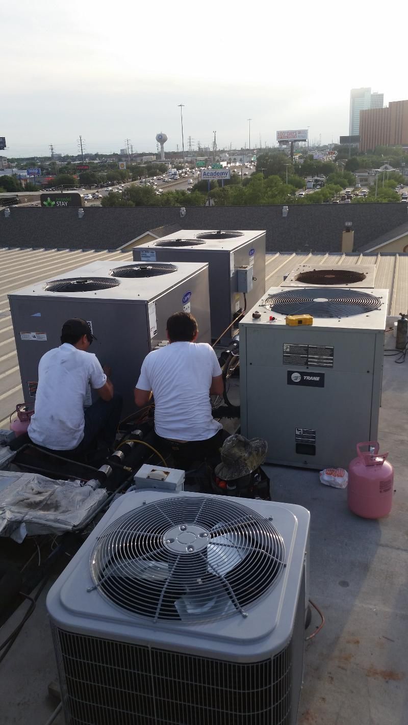 Two workers sit beside rooftop HVAC units, with city buildings and skyline in the background.