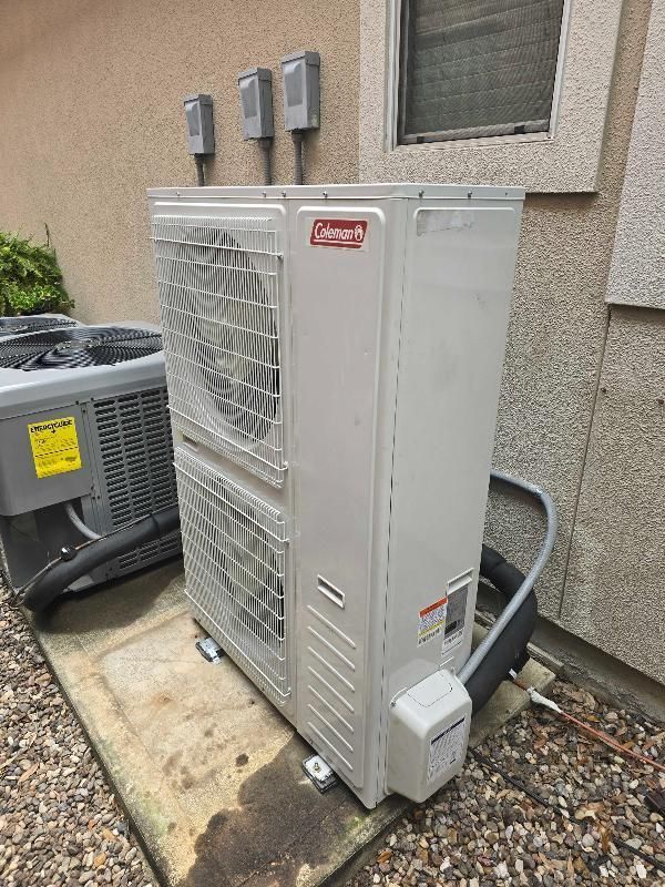 Outdoor HVAC heat pump unit beside a house, with utility lines and a window above it.