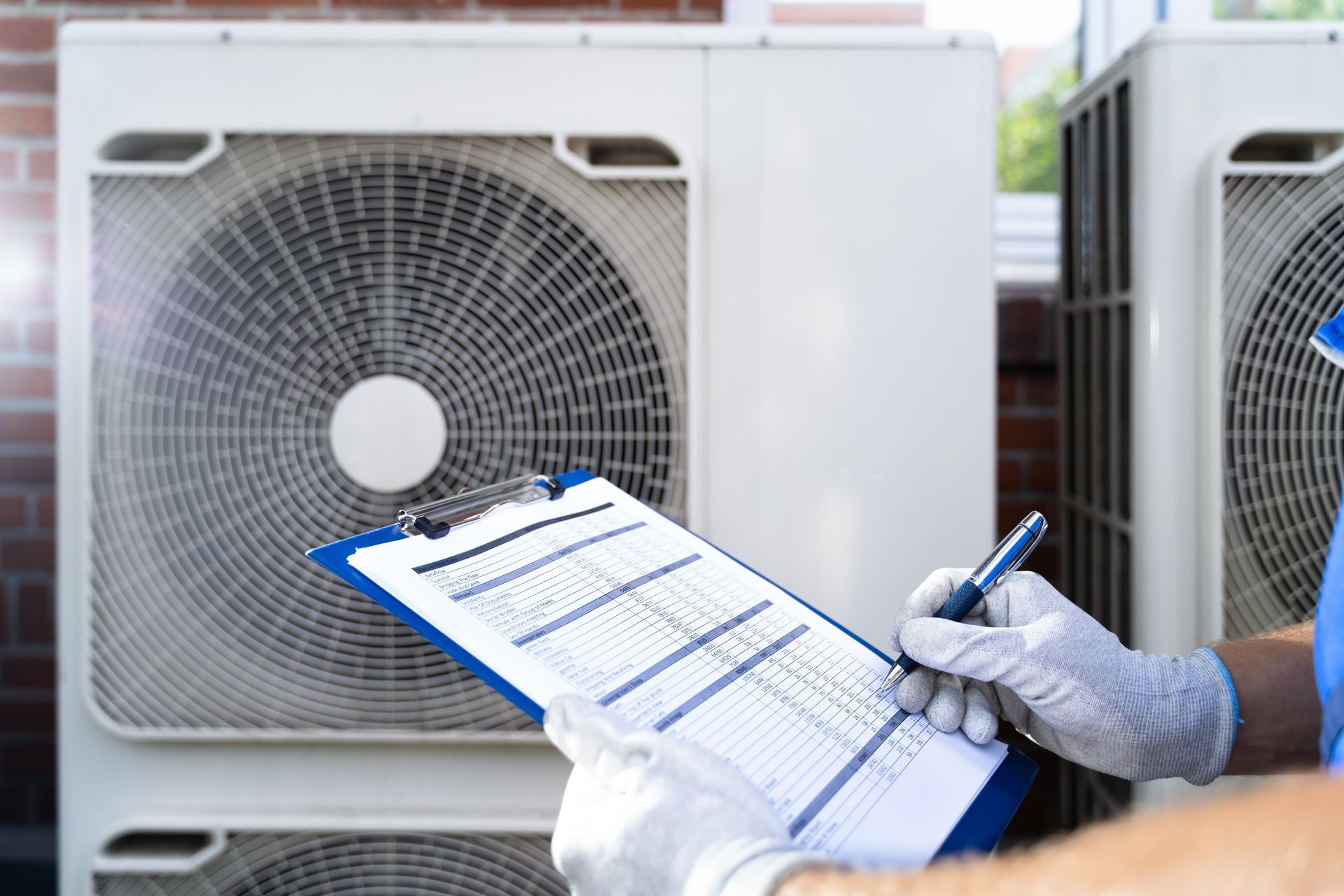 Technician in gloves checking HVAC units while writing on a clipboard