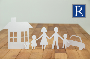 Paper cutouts of a family, house, car, and cat on wooden surface.