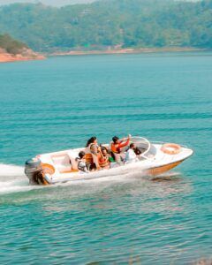 A motorboat speeds across a turquoise lake with several passengers, hills in the background.