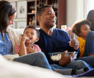 Family on a sofa, eating popcorn and smiling.