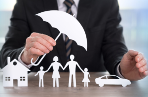 Man holding a paper umbrella over paper cutouts of a house, family, and car.
