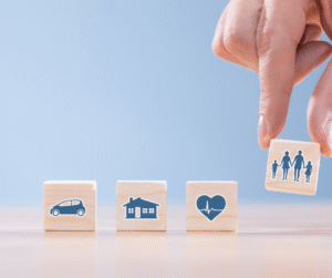 Hand placing family icon block next to car, house, and health insurance blocks.