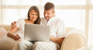 Couple sitting on a sofa looking at a laptop computer.