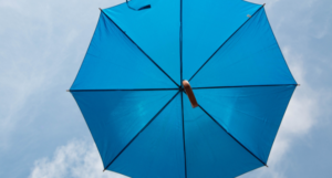 Blue umbrella against a cloudy sky, seen from below.