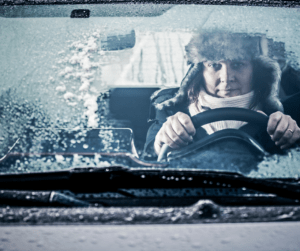 Person driving a car with an icy windshield; wearing a fur hat.