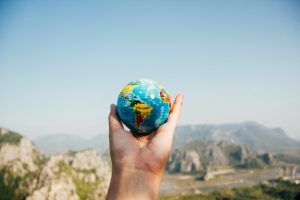 Hand holding a small globe against a blurry mountain range and blue sky.