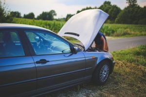 Blue car with open hood on the side of a rural road, person working under the hood.