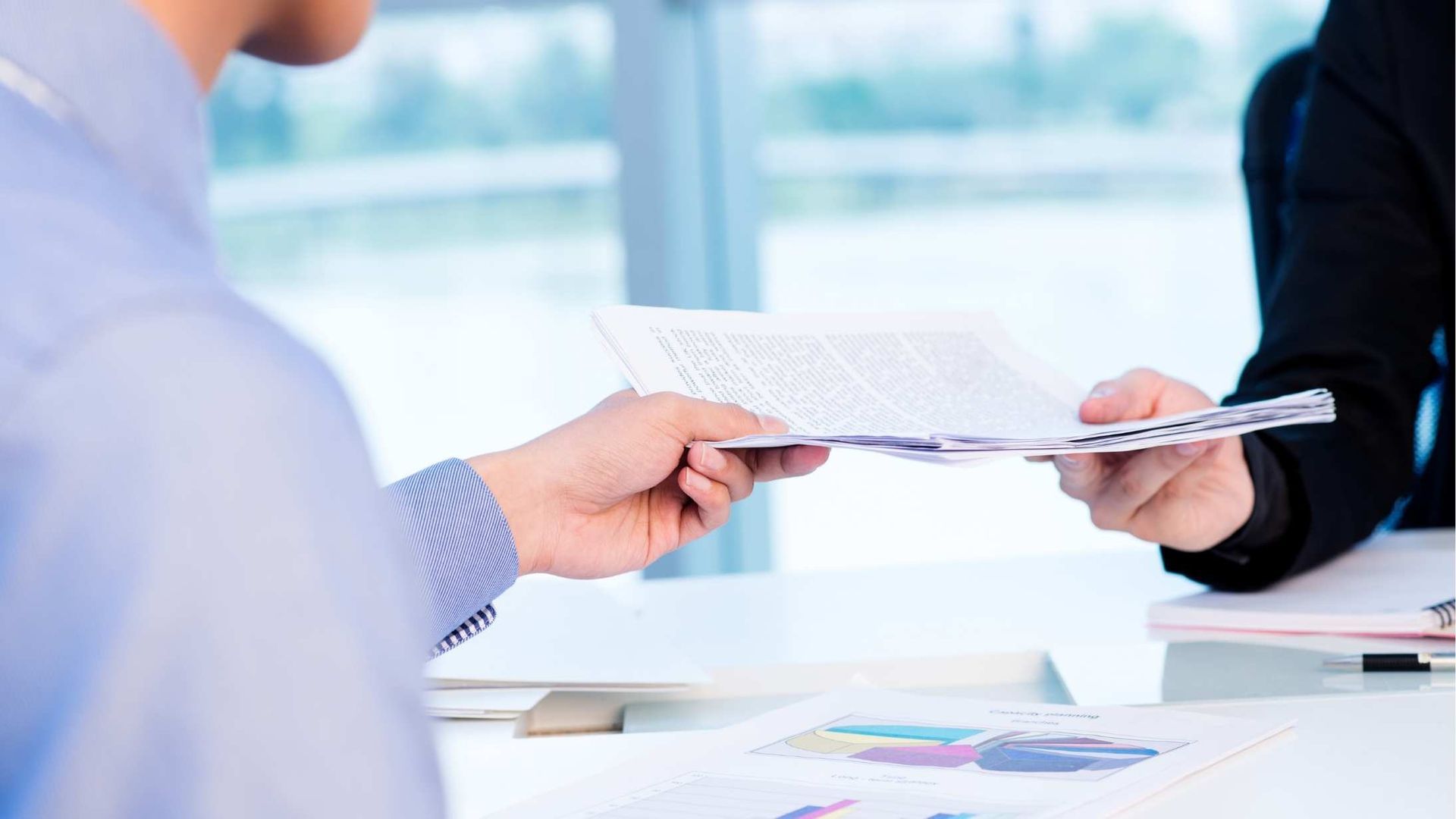 Hands exchanging a document across a bright office desk