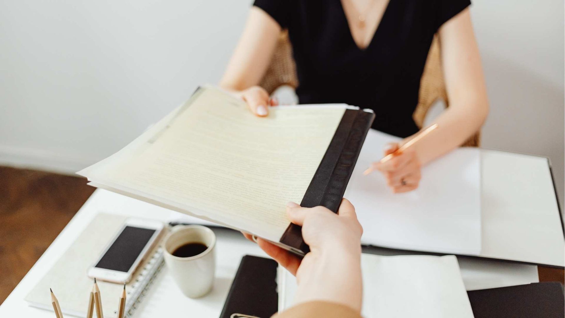 Person handing a notebook across a table in an office setting