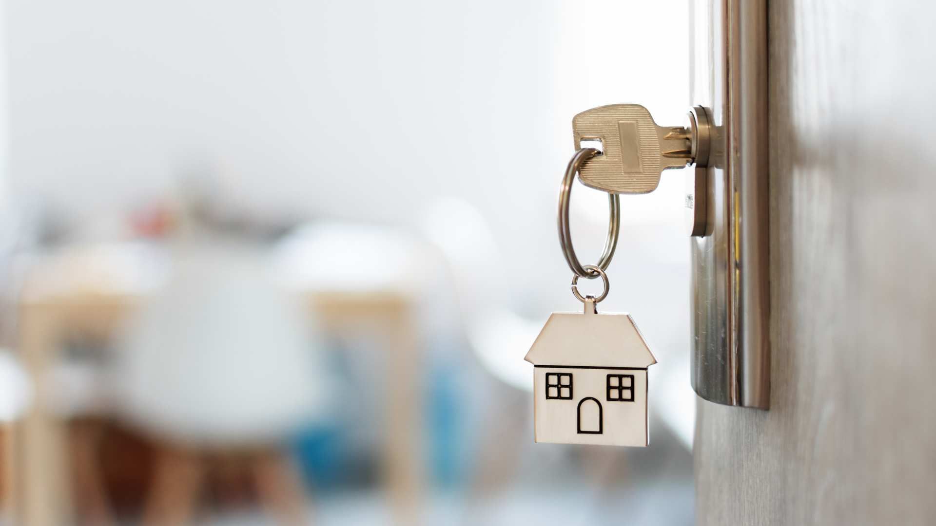 House-shaped keychain in a door lock with a blurred room in the background
