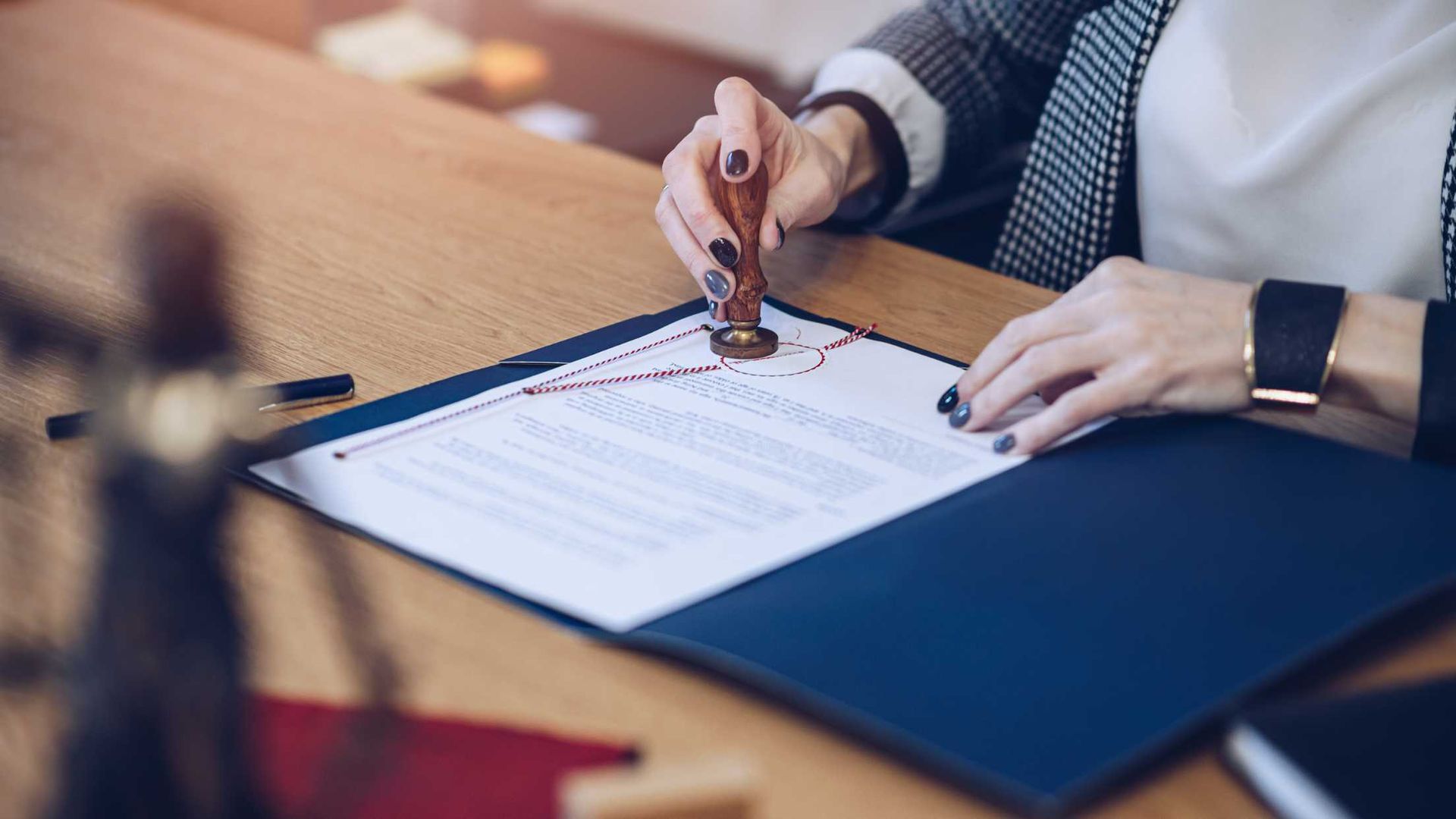 Hand signing a document on a blue folder at a wooden desk