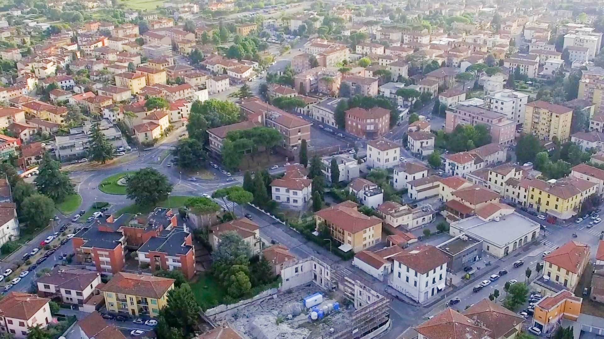 Aerial view of a dense city neighborhood with roads, trees, and many red-roofed buildings.